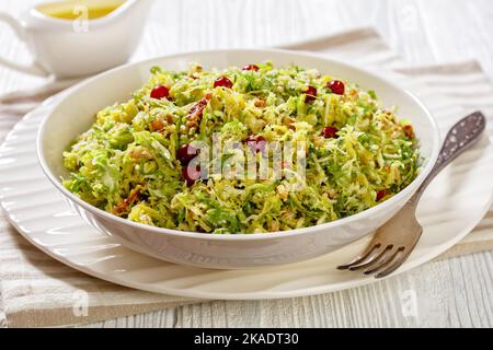 rosenkohl mit Mandeln, knusprigem gebratenem Speck und Preiselbeeren in einer weißen Schüssel auf einem Holztisch, horizontale Ansicht von oben, Nahaufnahme Stockfoto