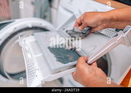 Horizontales Foto einer weiblichen Hand, die die Flusen aus dem schmutzigen Luftfilter der Färbemaschine herausnimmt Stockfoto