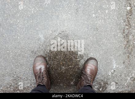 Wasserdichte Stiefel stehen auf rutschigem Eis auf der Straße Stockfoto