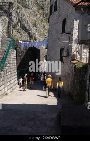 Kotor, Montenegro - 29. April 2022: Eine Gruppe von Touristen, die unter der Wäsche spazieren, die von mittelalterlichen Steinhäusern in einer engen Straße in der alten Kotor-Straße hängt Stockfoto