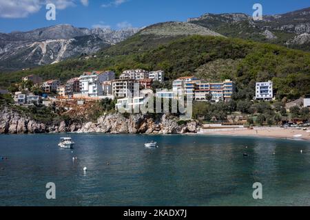 Budva, Montenegro - 28. April 2022: Adriaküste in der Region Budva. Sandstrand, türkisfarbenes Meerwasser, Hotelgebäude und Berge im Hintergrund. Stockfoto