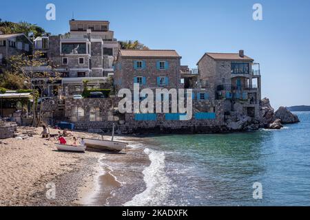 Budva, Montenegro - 28. April 2022: Malerische kleine Bucht am Przno Plaza. Sandstrand, mittelalterliche Stadtarchitektur. Stockfoto