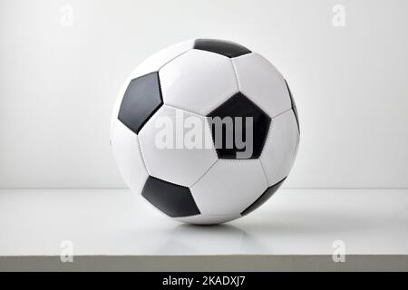 Detailansicht des klassischen schwarzen und weißen Lederfußballs isoliert auf grauem Tisch und hellem Hintergrund. Vorderansicht. Stockfoto