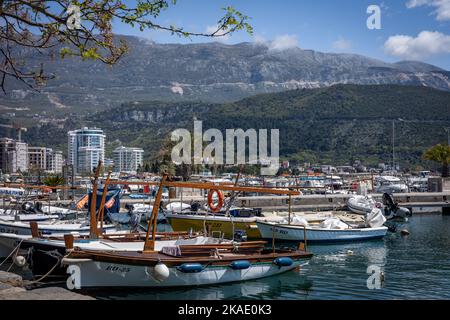 Budva, Montenegro - 28. April 2022: Kleine Fischerboote im Hafen von Budva. Sonniger Tag, Hotelgebäude und Berge im Hintergrund. Stockfoto