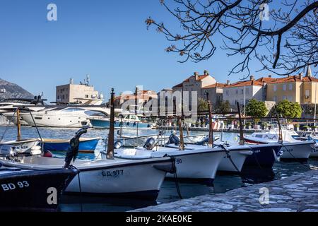 Budva, Montenegro - 28. April 2022: Kleine Fischerboote im Hafen von Budva. Sonniger Tag, mittelalterliche Zitadelle im Hintergrund. Stockfoto