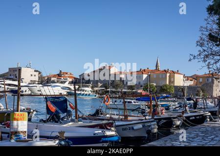 Budva, Montenegro - 28. April 2022: Kleine Fischerboote im Hafen von Budva. Sonniger Tag, mittelalterliche Zitadelle im Hintergrund. Stockfoto