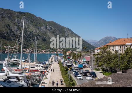 Kotor, Montenegro - 29. April 2022: Menschen auf einer Promenade in der Altstadt von Kotor, Boote und Schiffe liegen am Pier vor. Berge im Hintergrund.