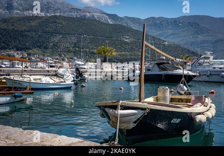 Budva, Montenegro - 28. April 2022: Kleine Fischerboote im Hafen von Budva. Sonniger Tag, Hotelgebäude und Berge im Hintergrund. Stockfoto