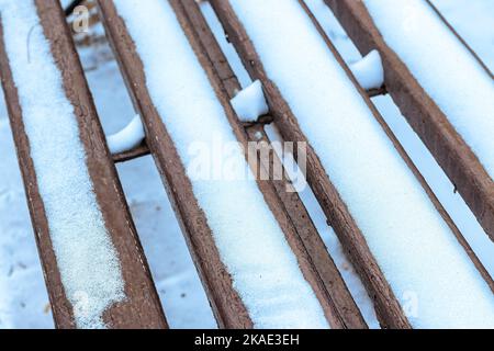 Eine Bank im Park im Winter mit Schnee bedeckt. Winterwetter und erster Schnee Konzept. Stockfoto