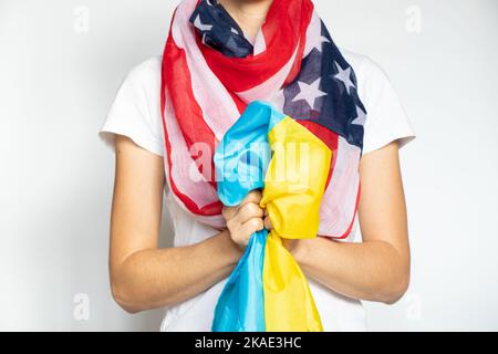 Ein Mädchen mit einer amerikanischen Flagge um den Hals hält eine ukrainische Flagge auf weißem Hintergrund, Amerika und die Ukraine zusammen, Gewerkschaft und Unterstützung im Krieg Stockfoto