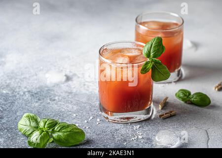 Tomatensaft oder Bloody Mary Eiscocktail mit Bazilblättern in zwei Gläsern für Getränkekarte auf blauem texturierten Hintergrund mit Textraum Stockfoto