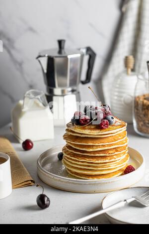 Stapel Pfannkuchen mit Honig und Beeren auf weißem Küchentisch. Konzept für das Frühstück am Morgen. Stockfoto