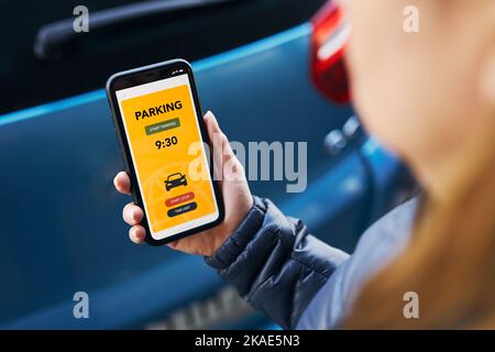 Frau nutzt die App für das mobile Parken auf dem Smartphone. Fahrer, der das Smartphone benutzt, um für das Parken zu bezahlen. Parkplatzanwendung auf dem Mobiltelefon. Convienience bezahlt für Stockfoto