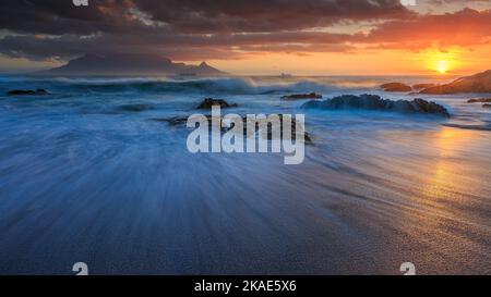 Zeitlupenwellen während eines stürmischen Sonnenuntergangs am Tafelberg vom Bloubergstrand aus Stockfoto