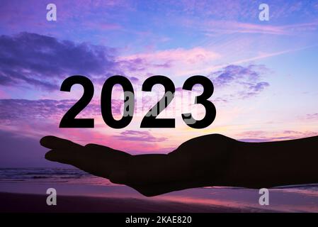 Hand bietet 2023 Zahlen, Sonnenuntergang Hintergrund, Neujahr Karte Stockfoto