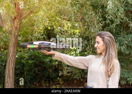 Seitenansicht einer jungen blonden Frau, die in der Natur mit einem Kopierraum herumschaut und eine riesige Drohne hält Stockfoto