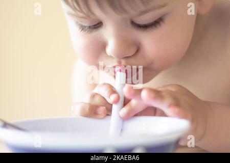 Niedlicher kleiner Junge, der mit Stroh aus einer Schüssel trinkt Stockfoto