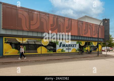 Finnland, Hamina - 18. Juli 2022: SS Market Lebensmittelgeschäft am Rande des zentralen Platzes unter blauer Wolkenlandschaft. Fußgänger gehen an Schaufenstern mit Baumstamm vorbei Stockfoto