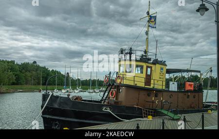 Finnland, Hamina - 18. Juli 2022: US-Militärschiff ST-79 des Zweiten Weltkriegs im Hafen unter grauer Wolkenlandschaft. Jachthafen und Grüngürtel hinten. Stockfoto