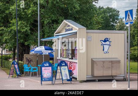 Finnland, Hamina - 18. Juli 2022: Beigefarbene Pingviini-Eishütte auf dem zentralen Platz. Grünes Laub als Hintergrund. Pinguin-Bild, Regenschirm und Cha Stockfoto