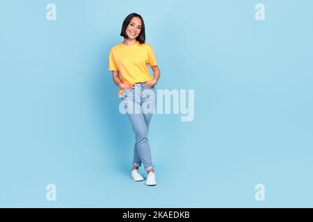 In voller Größe Foto von zufrieden schön niedlich girlish Frau tragen gelbe T-Shirt Denim Jeans Arme in der Tasche isoliert auf blauem Hintergrund Stockfoto