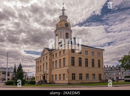 Finnland, Hamina - 18. Juli 2022: Seitenansicht, Stadt oder Rathaus aus gelbem Stein, Haminan raatihuone, mit Uhrenturm unter der grauen Wolkenlandschaft. Green la Stockfoto