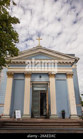 Finnland, Hamina - 18. Juli 2022: Vordereingang zur blauen St. Johns Kirche, Johanneksen kirkko, unter grauer Wolkenlandschaft. Dekorierte Säulen, offene Tür und Stockfoto