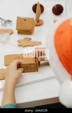 Ein Kind in einem Weihnachtsmütze macht ein Lebkuchenhaus. Neujahr. Ein Weihnachtsgeschenk Stockfoto