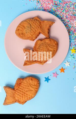 Die vertikale Draufsicht auf die fischförmigen Taiyaki-Eiszapfen in einer rosa Platte über der blauen Oberfläche Stockfoto