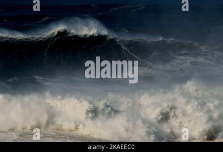 Ein wagemutiger Surfer reitet bei einem Surfwettbewerb in Nazaré, Portugal, eine riesige Welle. Die Großwellen-Saison in Nazare ist von Oktober bis März Stockfoto