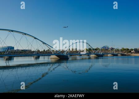 Ein Flugzeug am blauen Himmel über der Tempe Town Lake Fußgängerbrücke in Arizona. Stockfoto