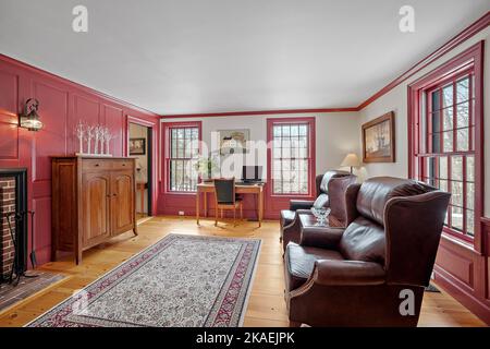 Ein gemütliches Wohnzimmer im Vintage-Stil mit Ledersesseln, Holzmöbeln und roten Fensterköpfen eingerichtet Stockfoto