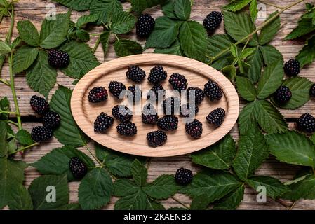 Frische reife Brombeeren in einer Holzschüssel mit grünen Blättern auf rustikalem Hintergrund. Flach liegend, Draufsicht. Stockfoto