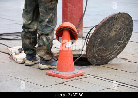 Arbeiter, der auf einer Straße über der offenen Kanalluke steht. Konzept der Reparatur von Abwasser, unterirdischen Versorgungseinrichtungen, Wasserversorgung, Kabelverlegung Stockfoto