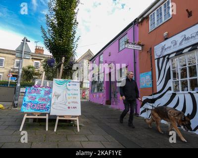 Ein Mann geht mit seinem Schäferhund die Straße hinunter an einem pinken Laden in Glastonbury in England vorbei Stockfoto