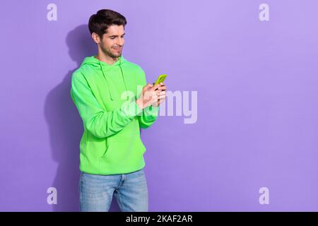 Foto von jungen Kerl tragen grünen Hoodie mit Smartphone online vdeo rufen leeren Raum ad facebook-Nutzer auf violetten Hintergrund isoliert Stockfoto