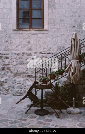 Eine vertikale Aufnahme eines kleinen runden Tisches mit leeren Stühlen auf der Straße. Montenegro. Stockfoto