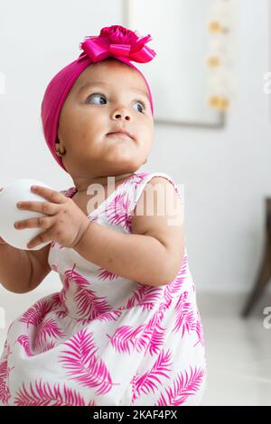 Braunhäutig Mädchen auf dem Boden sitzen spielen mit einer weißen Kugel. Mädchen, die nach hinten schauen. Stockfoto