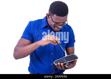 Ein hübscher junger Mann, der eine Brille trägt und sein Mobiltelefon mit einem Schraubendreher repariert. Stockfoto