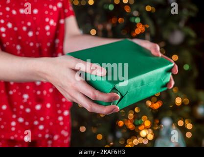 Hände präsentieren Weihnachtsgeschenkbox in grünem Geschenkpapier verpackt, Öko-Pack. Hochwertige Fotos Stockfoto