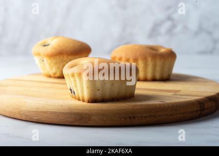 Drei hausgemachte Cupcakes auf einem hölzernen Schneidebrett. Fokus im Vordergrund. Stockfoto