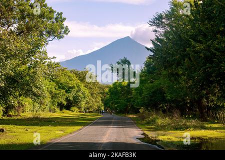 Eine Straße umgeben von viel Grün mit dem Mombacho Vulkan in der Ferne in Nicaragua Stockfoto
