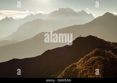 Ein Mann steht auf einem Panoramagipfel am Giau-Passo in der warmen Hintergrundbeleuchtung vor Bergketten und dem Berg Marmolada, Dolomiten, Italien Stockfoto