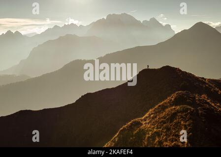 Ein Mann steht auf einem Panoramagipfel am Giau-Passo in der warmen Hintergrundbeleuchtung vor Bergketten und dem Berg Marmolada, Dolomiten, Italien Stockfoto