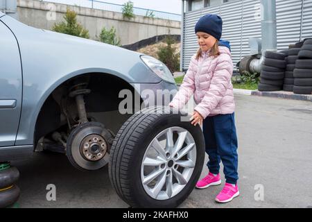 Kleines Mädchen in einem Autoservice, über den Austausch von Radreifen und die Wartung einer Fahrzeugaufhängung. Auto-Reparatur-Konzept Stockfoto