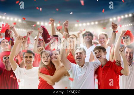 Fußballfan im Stadion in rot-weißem Hemd. Fröhliche Fans auf dem Fußballfeld, die das siegreiche Mannschaftsspiel beobachten. Gruppe von Unterstützern mit Flagge Stockfoto