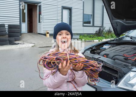 Ein kleines Mädchen mit einem Draht in den Händen arbeitet in der Garage. Autoservice Stockfoto