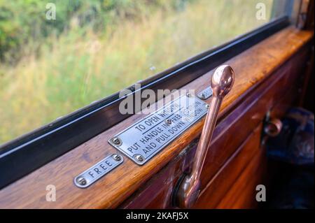 Ein alter Handhebel zum Öffnen und Schließen eines Wagenfensters in einem alten Dampfzug auf der Bluebell Railway in East Sussex, England. Stockfoto