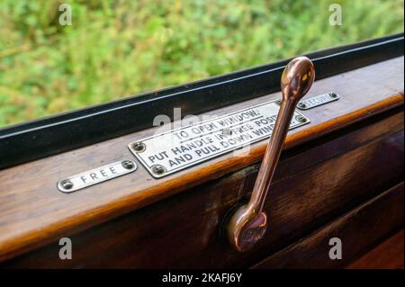 Ein alter Handhebel zum Öffnen und Schließen eines Wagenfensters in einem alten Dampfzug auf der Bluebell Railway in East Sussex, England. Stockfoto
