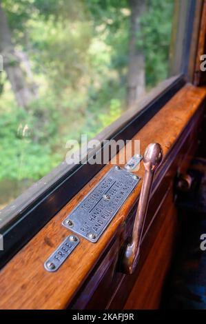 Ein alter Handhebel zum Öffnen und Schließen eines Wagenfensters in einem alten Dampfzug auf der Bluebell Railway in East Sussex, England. Stockfoto